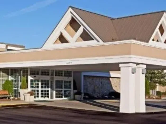 Envision Hotel, a beige building featuring a prominent triangular roof gable and a covered entrance driveway supported by double large white columns.
