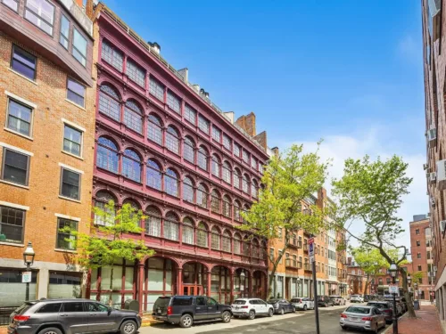 Fulton Street Condos, a five-story, maroon historic building with distinct architectural features, including repeating arched windows and a ground floor of large glass storefronts.