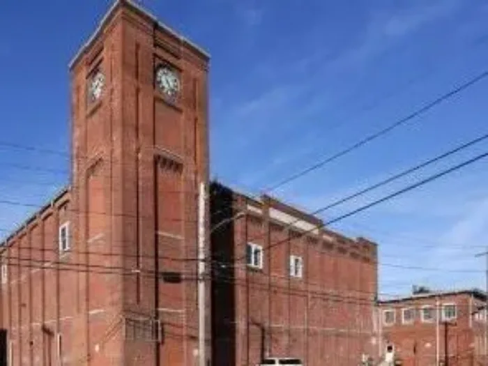 A low-angle of Hathaway Mills, a large industrial-style red brick building with a large clock tower rising on the left side.