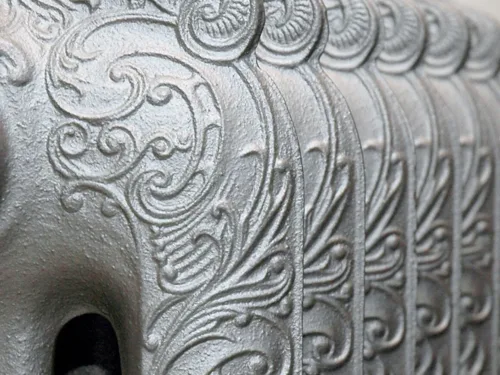 A close-up of a ornate, cast-iron radiator with embossed swirling patterns.