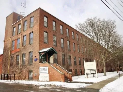 A low-angle of Stationary Factory, a long three and a half story red brick building with a covered entrance at the top of a staircase.