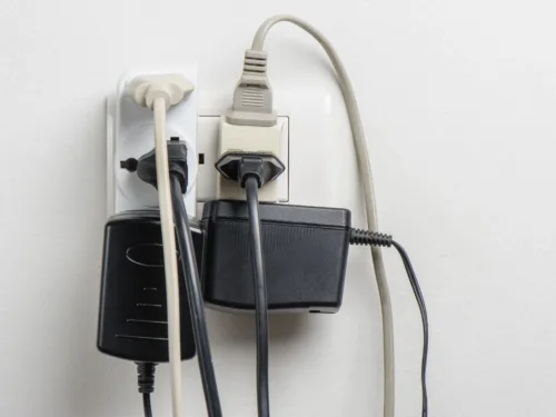 A wall outlet overloaded with multiple plugs and large power adapters.