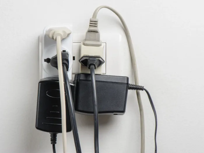 A wall outlet overloaded with multiple plugs and large power adapters.