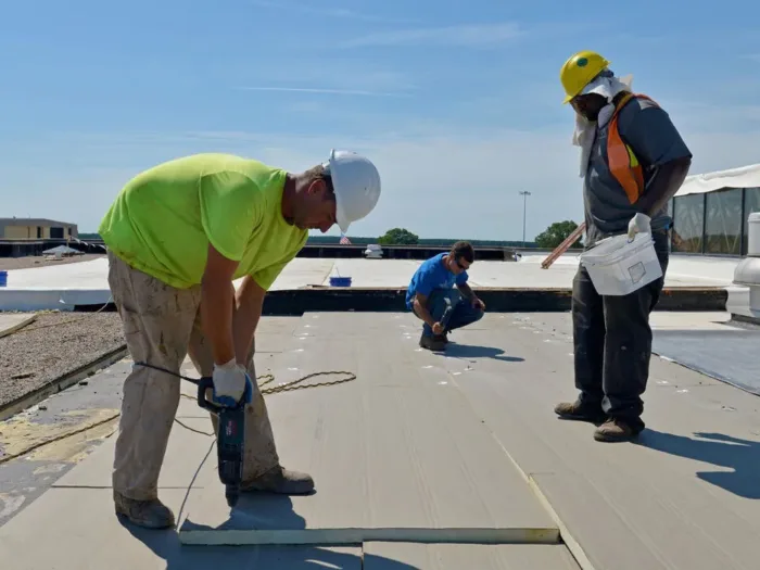 A roofing crew working together to install insulation panels on a large commercial roof.
