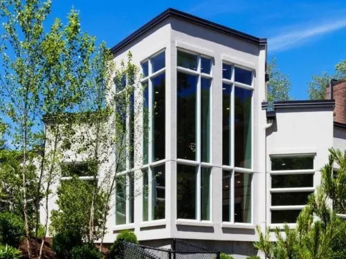 A low-angle view of Temple Beth Avodah, a contemporary white building featuring tall, multi-paned windows that wrap around the pointed central facade.