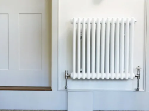 A classic white column radiator mounted on a white wall with a silver valve on the right.