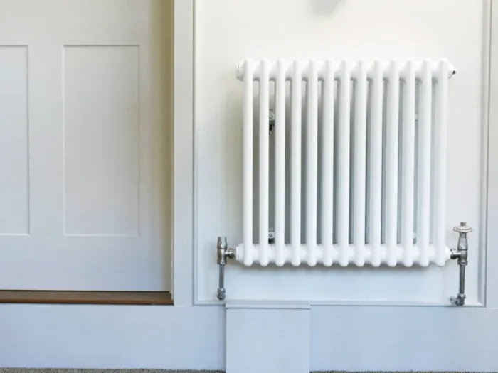 A classic white column radiator mounted on a white wall with a silver valve on the right.