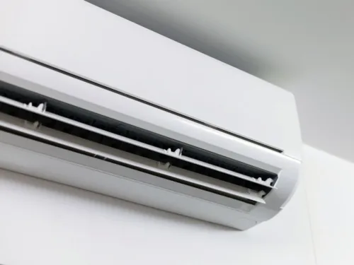 A close-up of a modern, white, ductless mini-split heat pump mounted on a white wall.