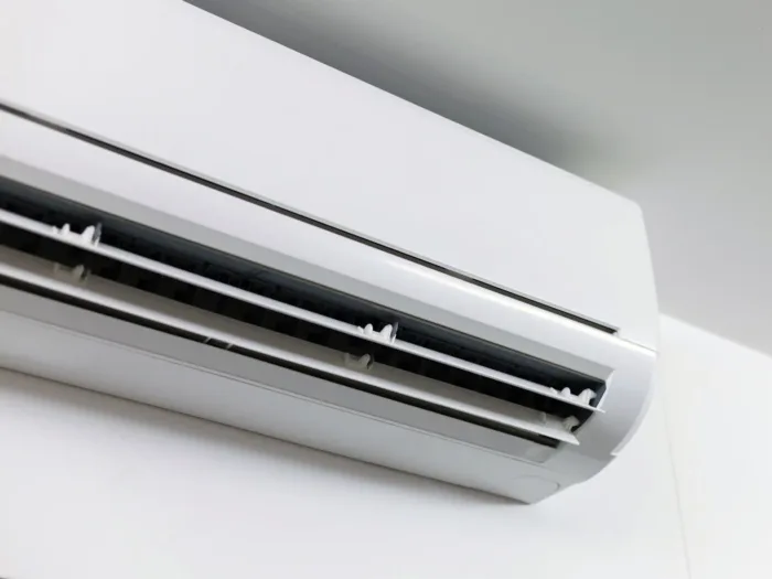 A close-up of a modern, white, ductless mini-split heat pump mounted on a white wall.