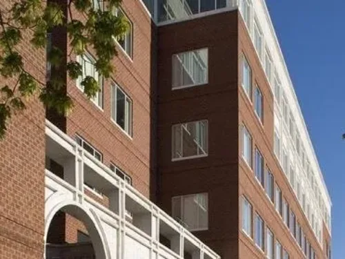 A low-angle of Waltham Healthcare, a red brick building featuring a white, arched architectural element in the foreground, and numerous windows reflecting the sky.