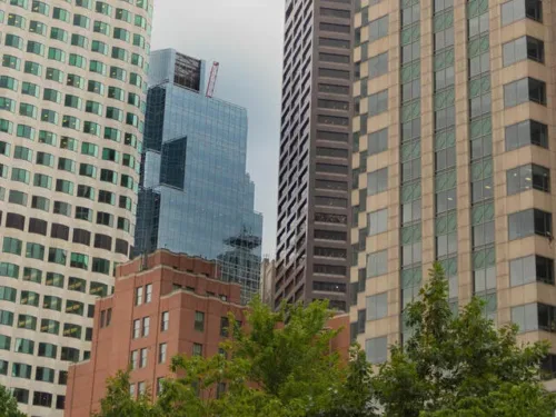 A low-angle view of several tall skyscrapers in a city, with green trees in the foreground.