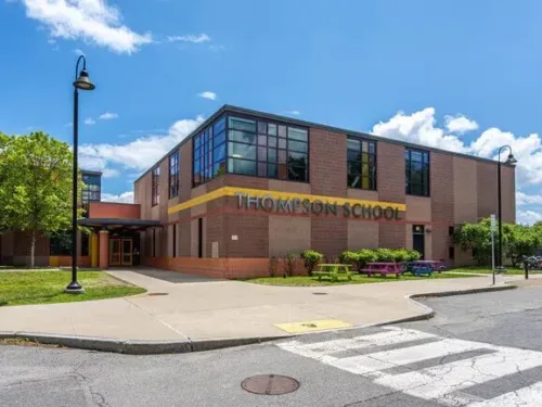 A wide shot of Thompson School featuring a brick facade, a yellow horizontal accent strip at level two height, and large windows.